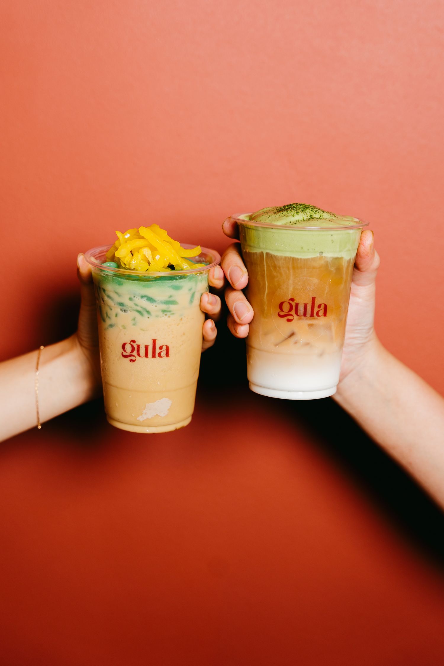 Three palm-sugar iced drinks held up against gula's terracotta wall